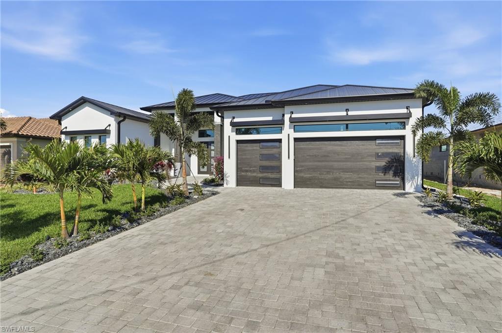 View of front of property with decorative driveway, an attached garage, a metal roof, and stucco siding