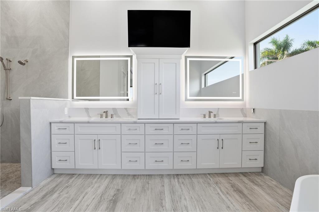 Full bathroom featuring double vanity, tile walls, walk in shower, and light wood-style floors