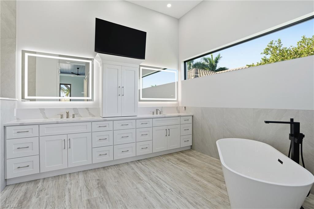 Bathroom with double vanity, a freestanding tub, light wood-style flooring, and tile walls
