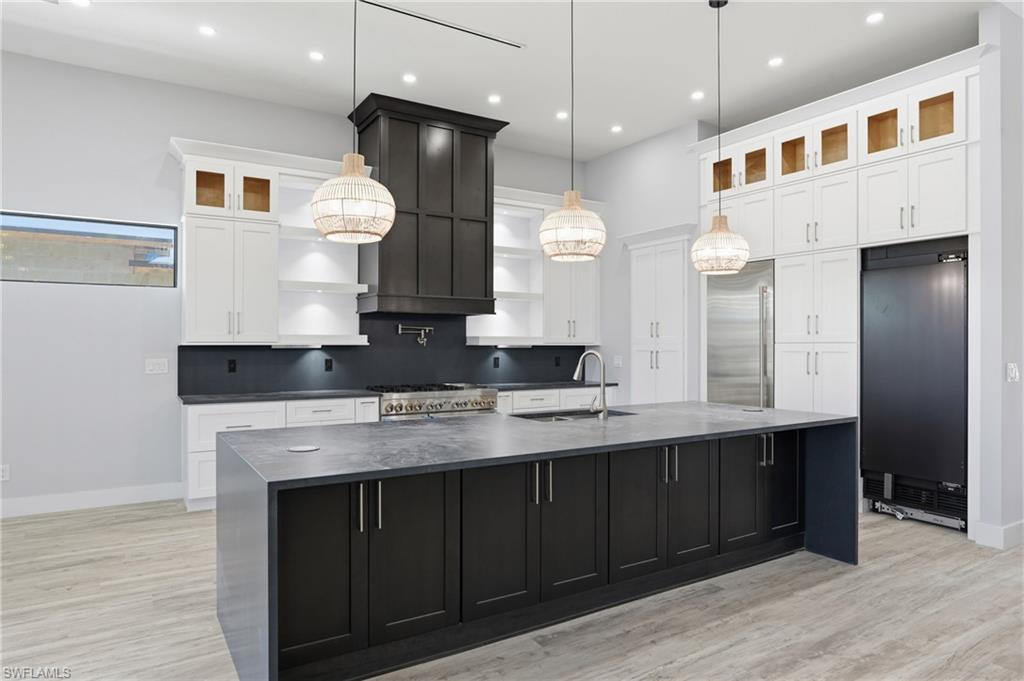Kitchen featuring dark cabinets, glass insert cabinets, a large island with sink, white cabinetry, and light wood-type flooring