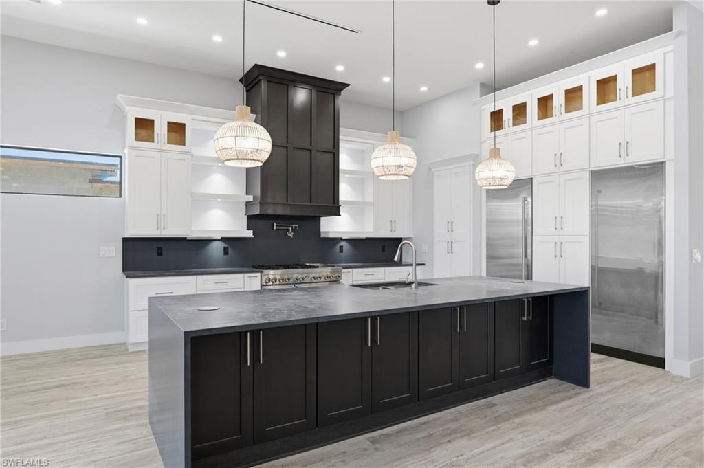 Kitchen with dark cabinetry, glass insert cabinets, white cabinets, a large island, and light wood-type flooring