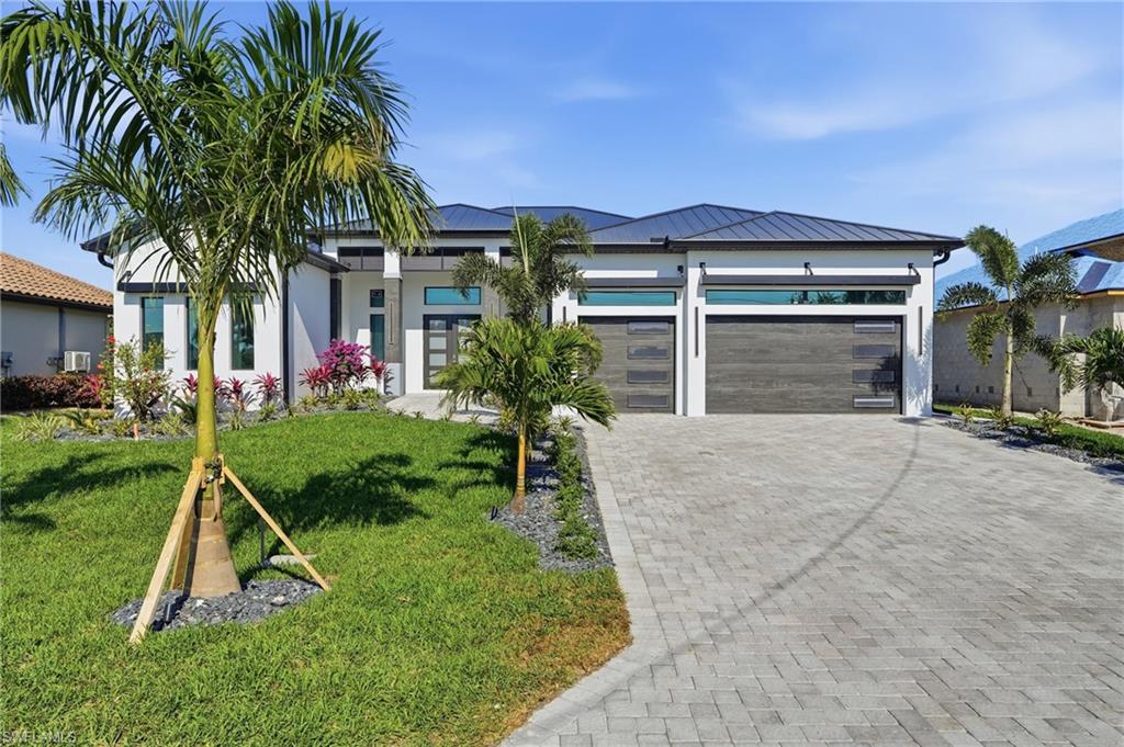 View of front of home featuring decorative driveway, a garage, a front lawn, a metal roof, and a standing seam roof