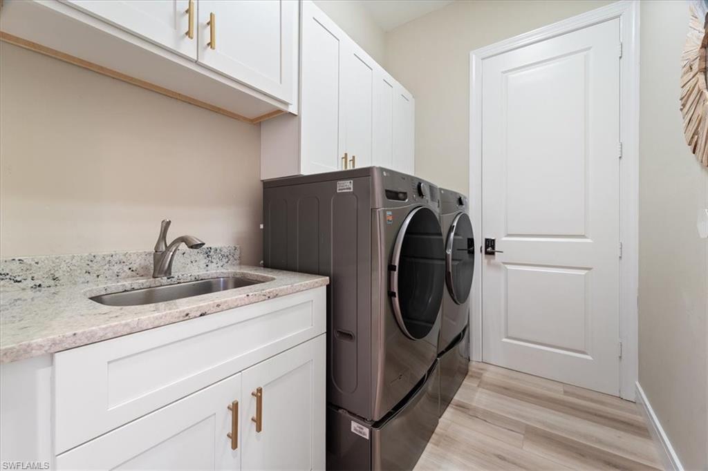 Laundry area with light wood-style flooring, independent washer and dryer, a sink, and cabinet space