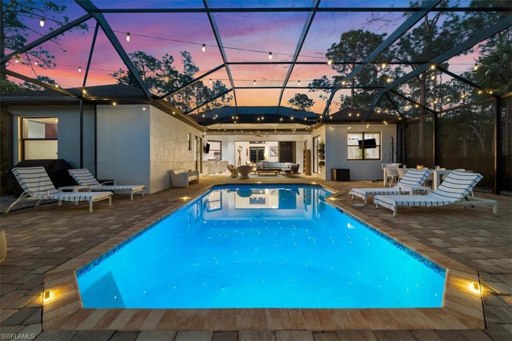 Pool at dusk featuring an outdoor pool, a patio area, and glass enclosure