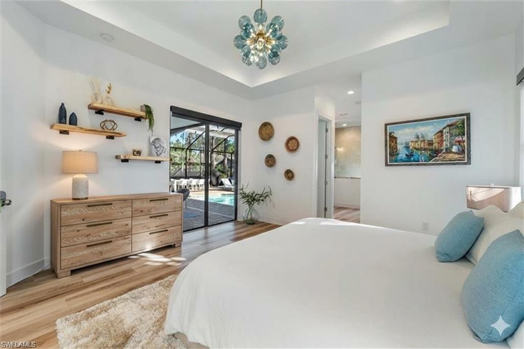 Bedroom featuring light wood-style floors, access to exterior, a raised ceiling, and recessed lighting