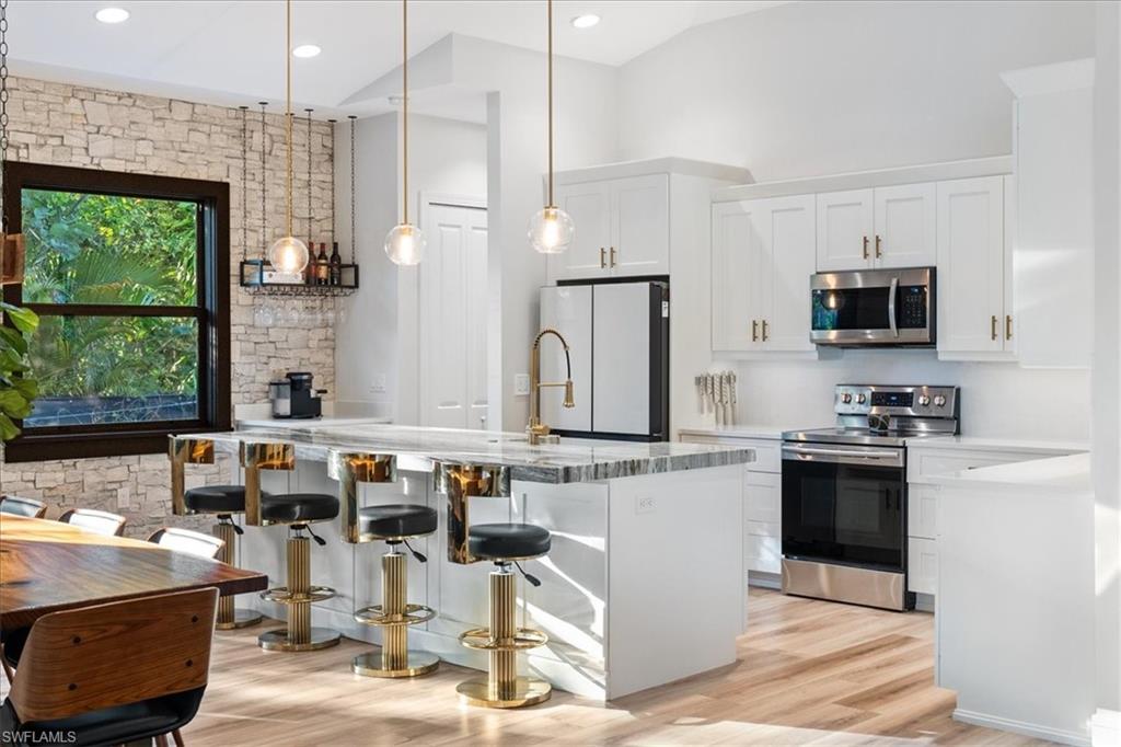 Kitchen featuring white cabinetry, a breakfast bar area, appliances with stainless steel finishes, light wood finished floors, and hanging light fixtures