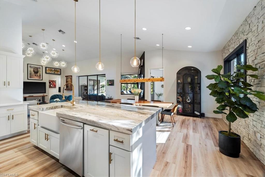 Kitchen with light wood-style flooring, white cabinets, dishwasher, a sink, and a center island with sink