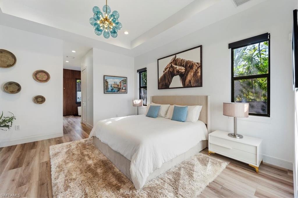 Bedroom with a tray ceiling, recessed lighting, baseboards, and light wood-style flooring