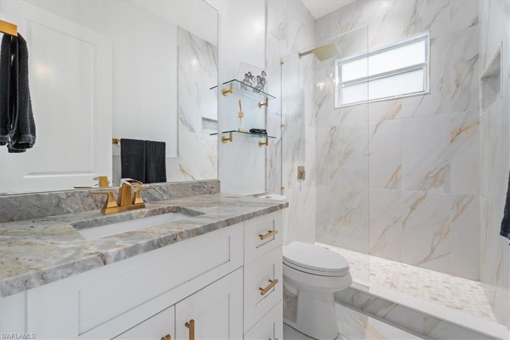 Bathroom with a marble finish shower, toilet, marble finish floor, and vanity