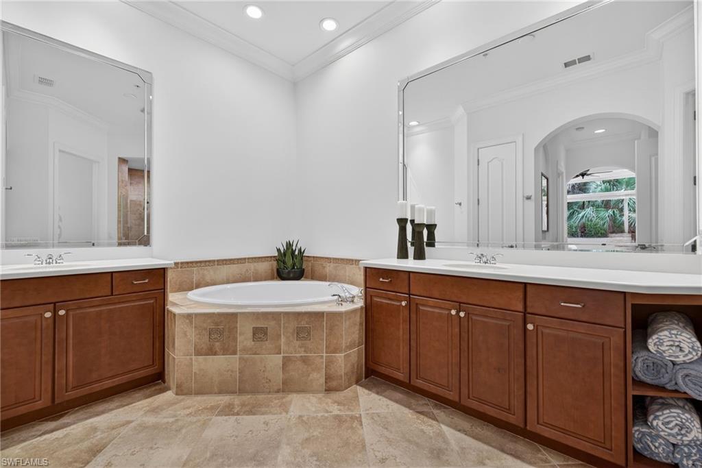 Full bath with two vanities, crown molding, a garden tub, and recessed lighting