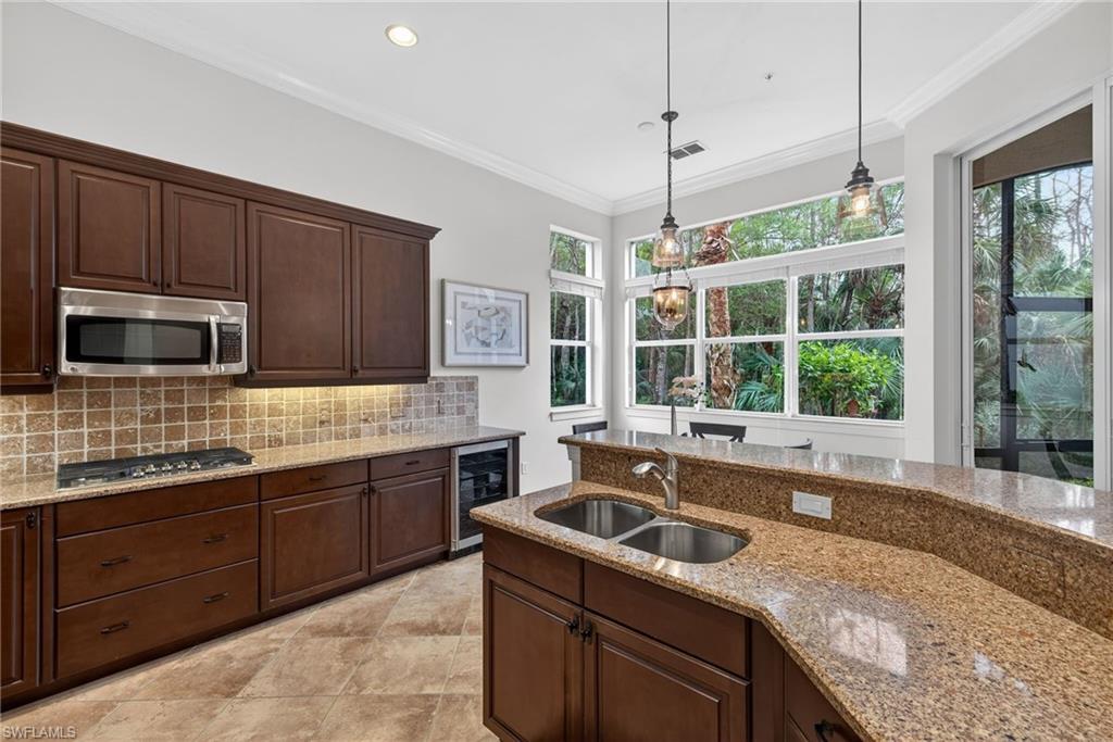 Kitchen with ornamental molding, hanging light fixtures, dark brown cabinets, light stone counters, and stainless steel appliances