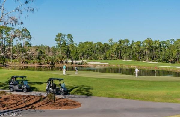 View of community featuring view of golf course, a yard, view of wooded area, and a water view