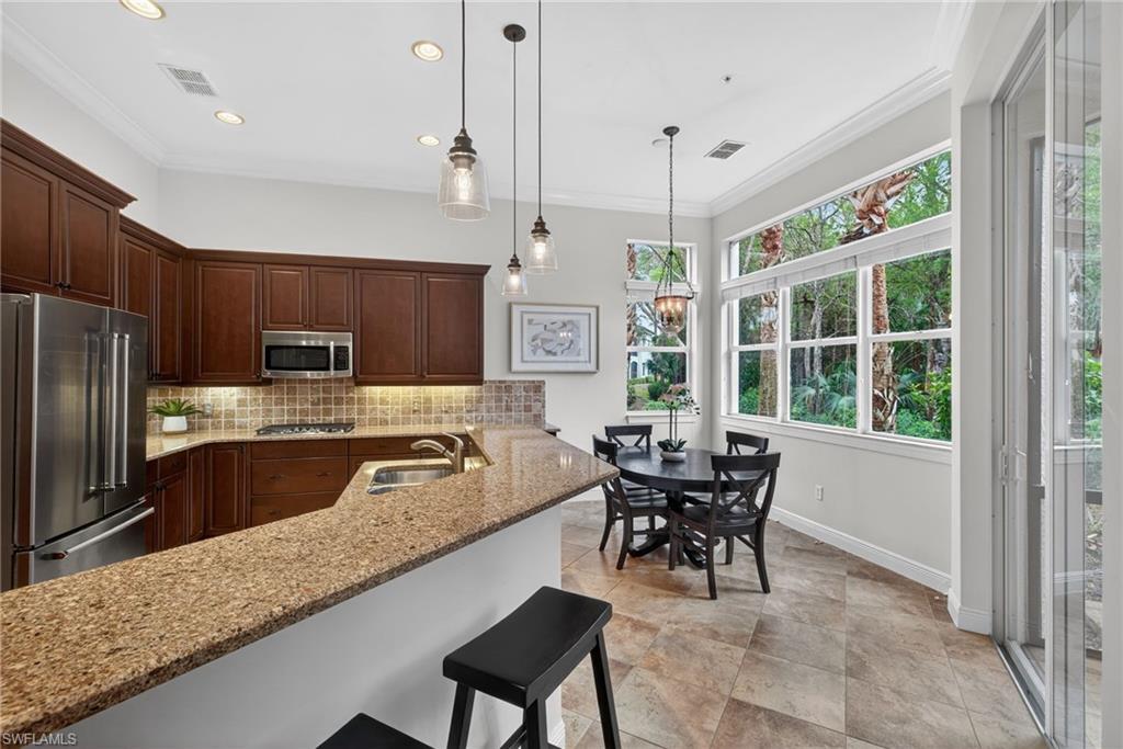 Kitchen featuring stainless steel appliances, light stone countertops, ornamental molding, a breakfast bar area, and pendant lighting