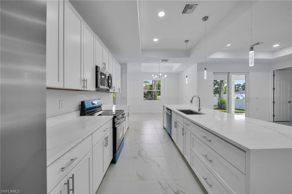 Kitchen with a raised ceiling, appliances with stainless steel finishes, white cabinets, light stone counters, and pendant lighting