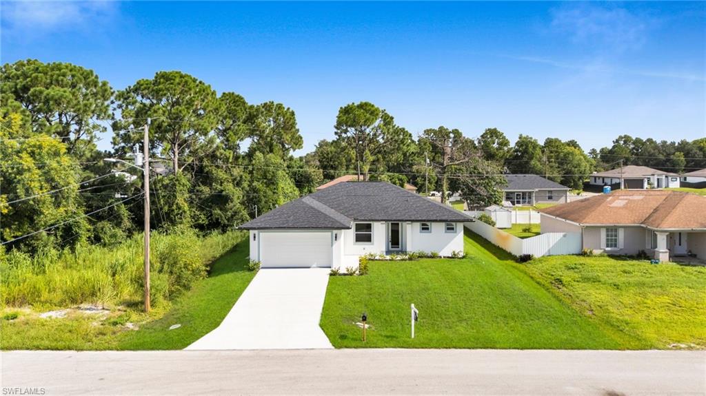 View of front of house featuring concrete driveway, a garage, stucco siding, view of scattered trees, and a shingled roof