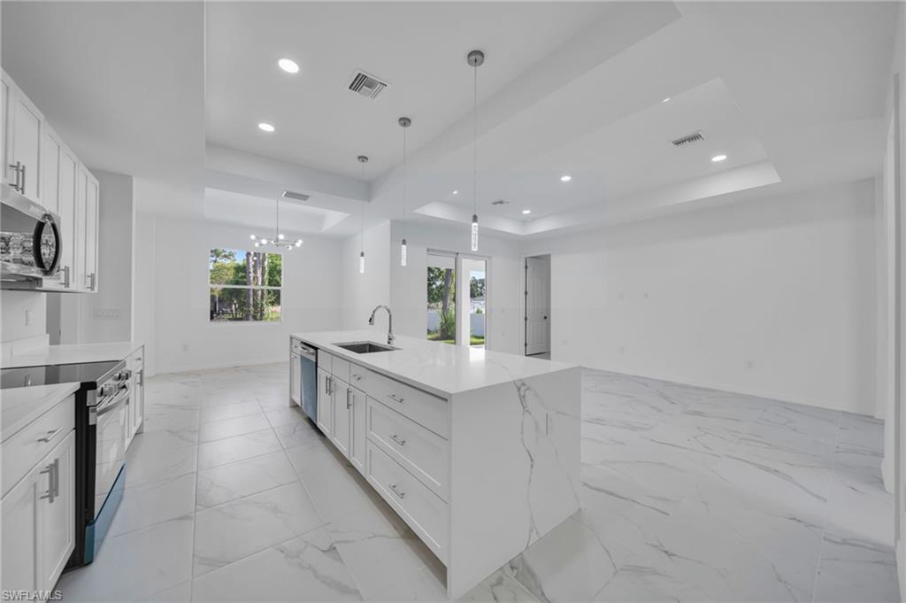Kitchen with white cabinets, a tray ceiling, appliances with stainless steel finishes, light stone countertops, and decorative light fixtures