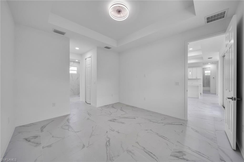 Empty room featuring a tray ceiling, recessed lighting, and light marble finish floors