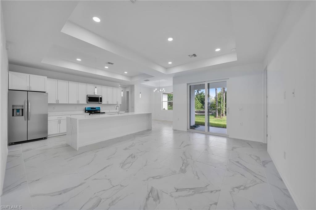 Kitchen featuring stainless steel appliances, open floor plan, white cabinetry, an island with sink, and light stone countertops
