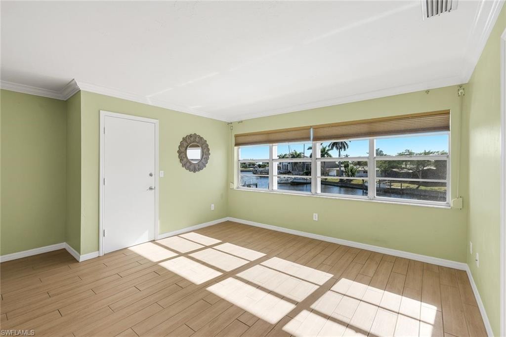 Unfurnished room featuring wood finish floors, a water view, and ornamental molding