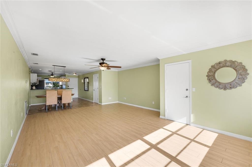 Unfurnished living room with light wood-style flooring, ornamental molding, and a ceiling fan