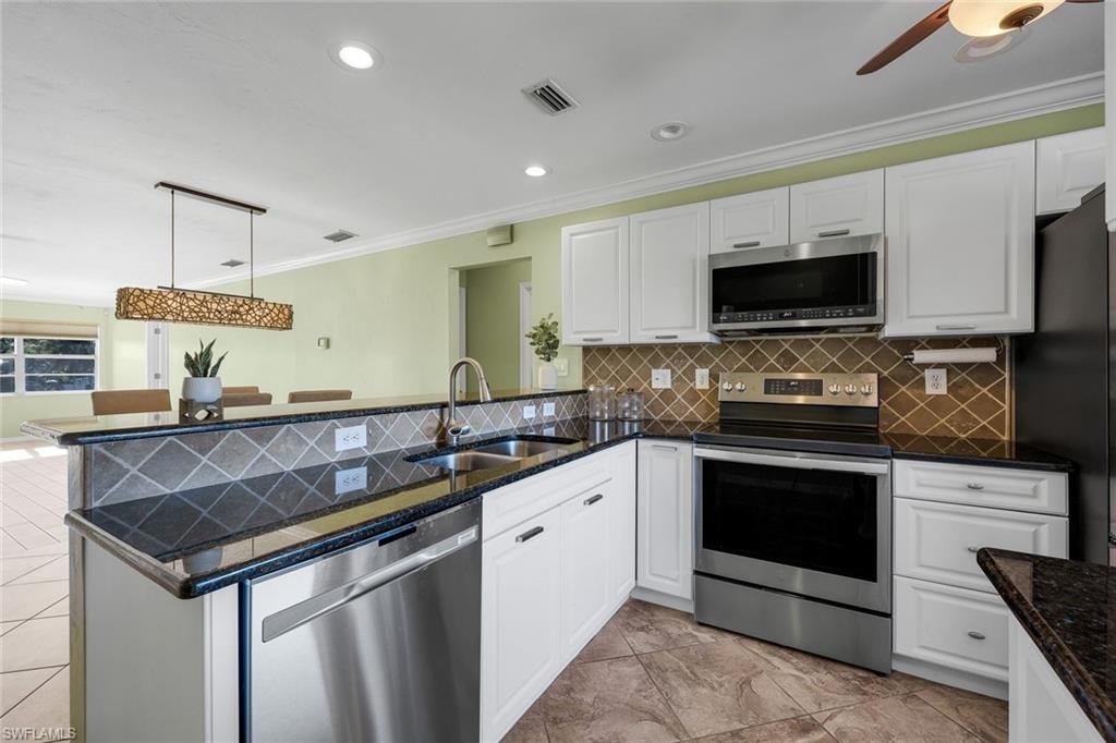 Kitchen with stainless steel appliances, ornamental molding, decorative light fixtures, white cabinetry, and backsplash