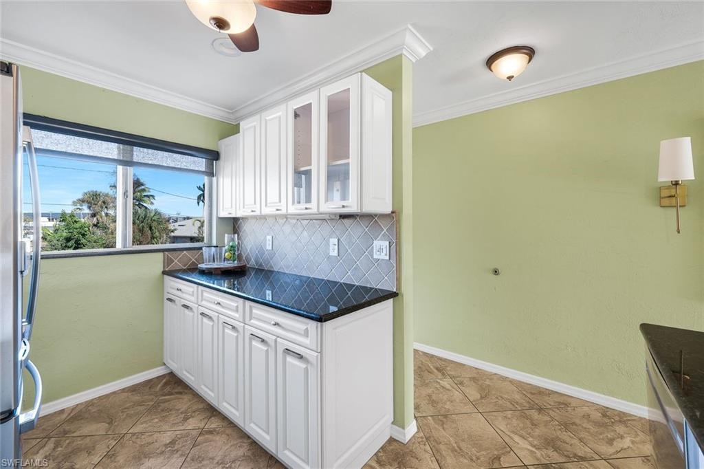 Kitchen featuring white cabinetry, glass insert cabinets, ornamental molding, tasteful backsplash, and freestanding refrigerator