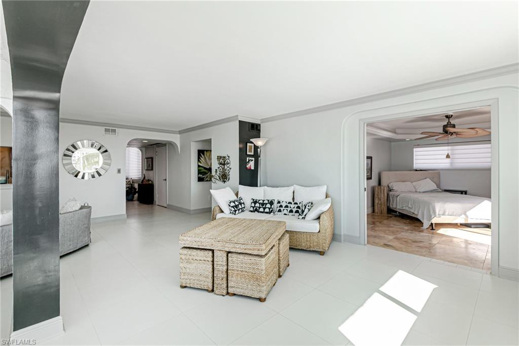 Living room featuring arched walkways, a ceiling fan, crown molding, and light tile patterned floors
