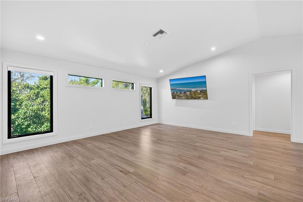 Bright living area with large windows, lofted ceiling, recessed lighting, and light wood floors.