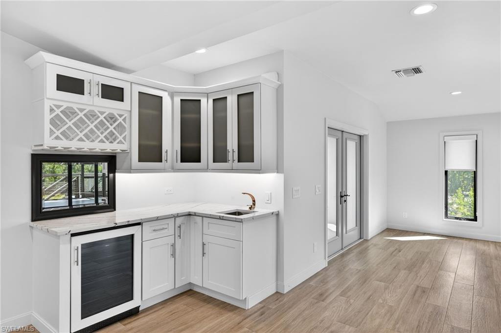 Bar area featuring wine fridge, bar sink, custom cabinetry, glass storage