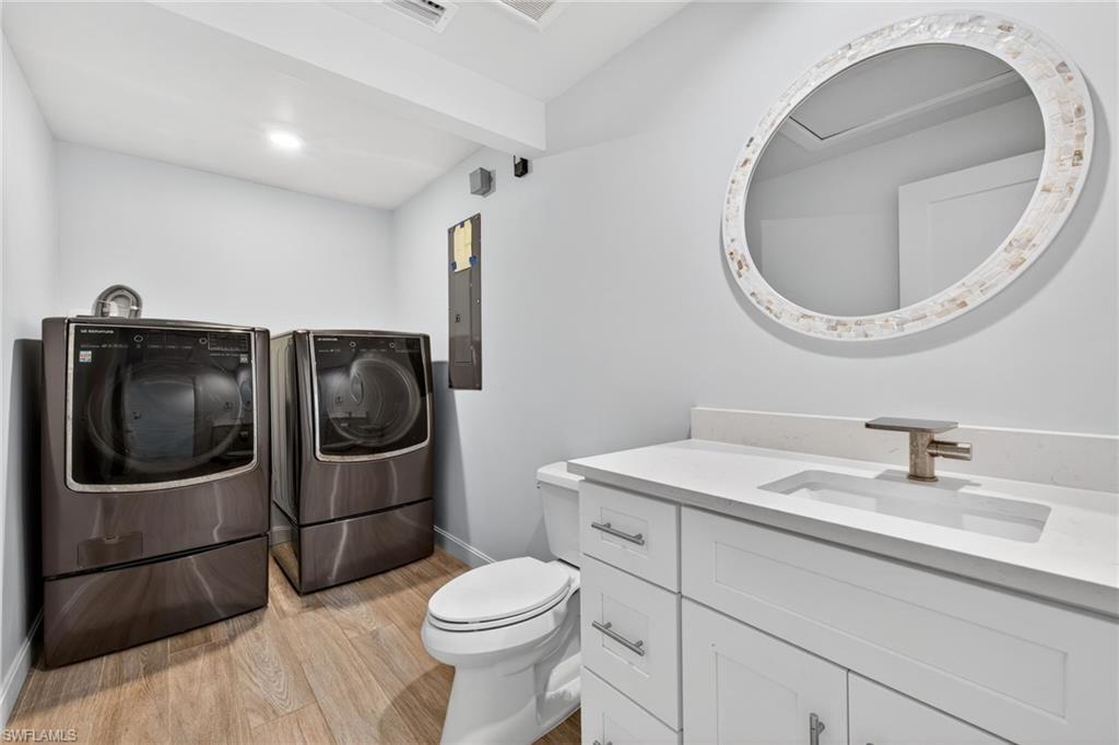 Bathroom featuring vanity, washing machine and dryer, light wood finished floors, beam ceiling, and electric panel