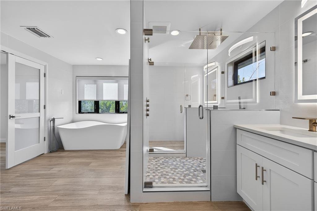 Dual door rainfall shower stall, modern soaking tub, designer tile, backlit mirrors, natural light.