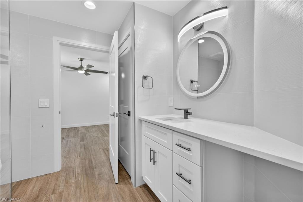 Bathroom with vanity, light wood-type flooring, a ceiling fan, recessed lighting, and tile walls