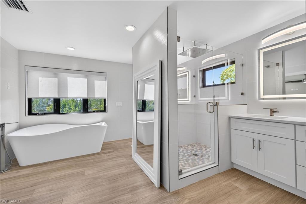 Dual door rainfall shower stall, modern soaking tub, designer tile, backlit mirrors, natural light.