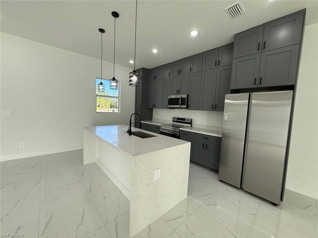 Kitchen with appliances with stainless steel finishes, decorative light fixtures, gray cabinetry, light stone counters, and light marble finish floors