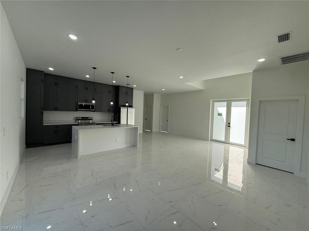 Kitchen with open floor plan, an island with sink, decorative light fixtures, stainless steel appliances, and light marble finish floors