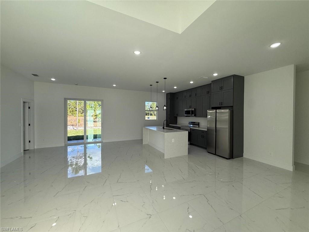 Kitchen featuring open floor plan, appliances with stainless steel finishes, pendant lighting, a center island with sink, and recessed lighting