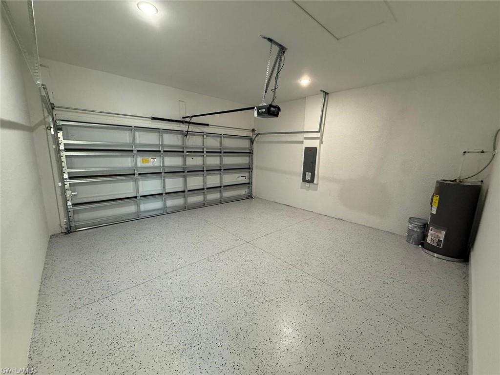 Garage with water heater, electric panel, recessed lighting, and a garage door opener
