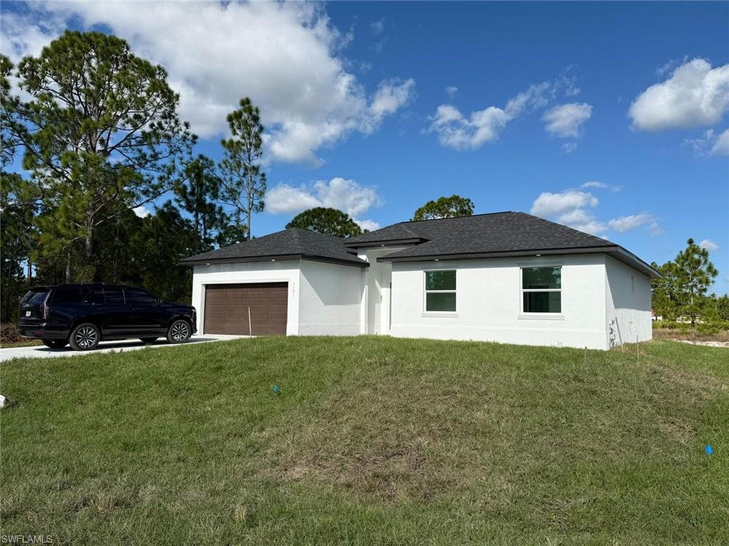 View of front of house with stucco siding, a front lawn, an attached garage, and concrete driveway