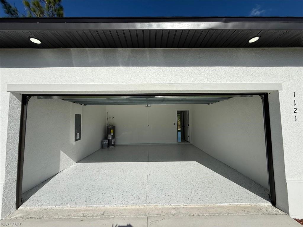 Garage with a textured wall, electric panel, water heater, and recessed lighting