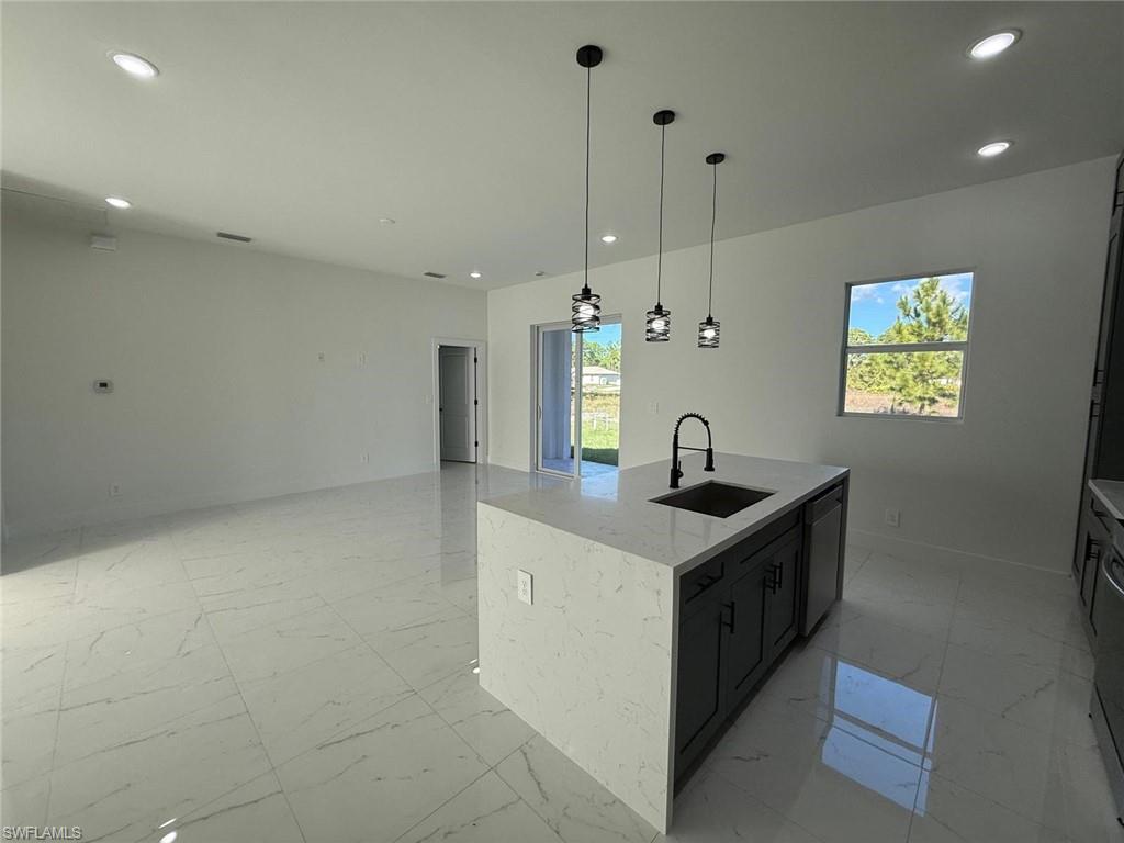 Kitchen featuring open floor plan, light stone counters, pendant lighting, dark cabinetry, and recessed lighting
