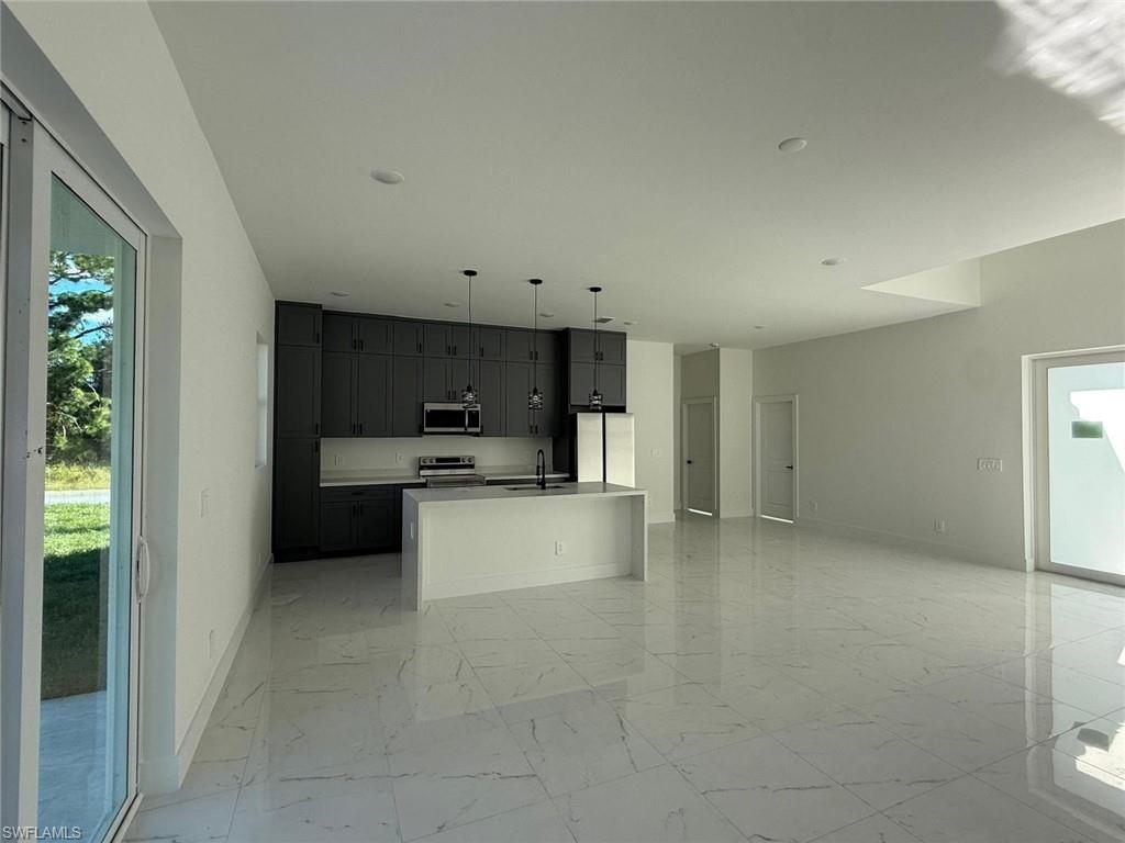 Kitchen with a center island with sink, pendant lighting, open floor plan, appliances with stainless steel finishes, and light marble finish floors