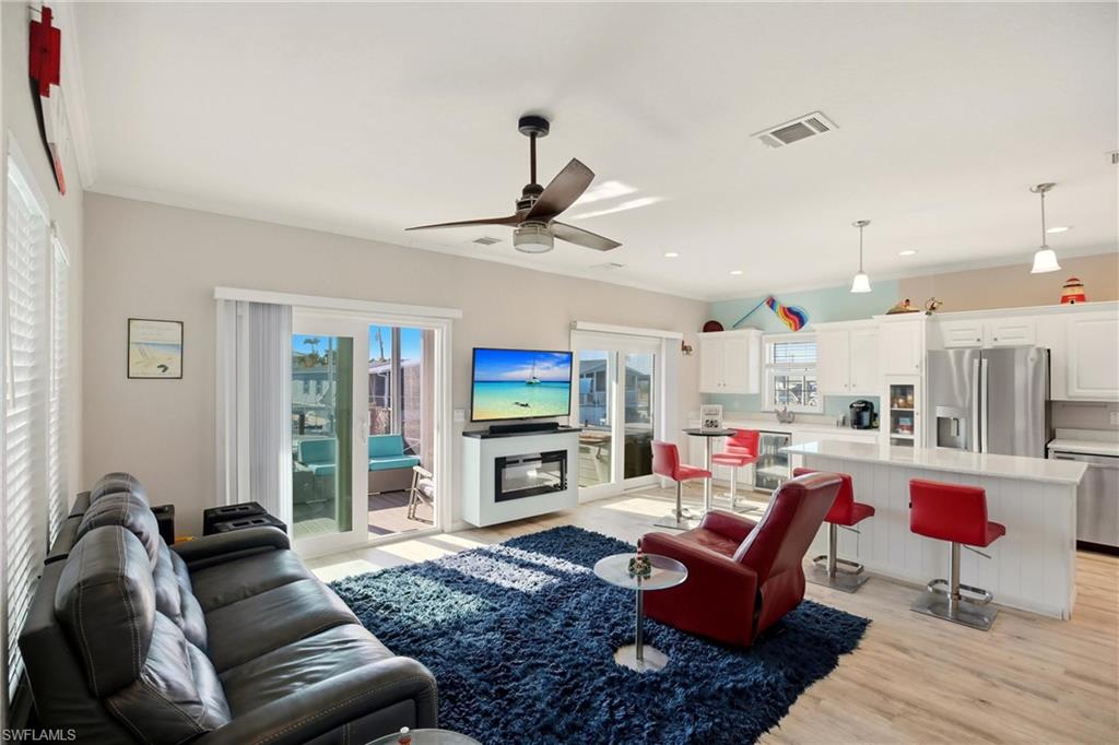 Living room featuring light wood-style floors, a glass covered fireplace, wine cooler, recessed lighting, and ceiling fan