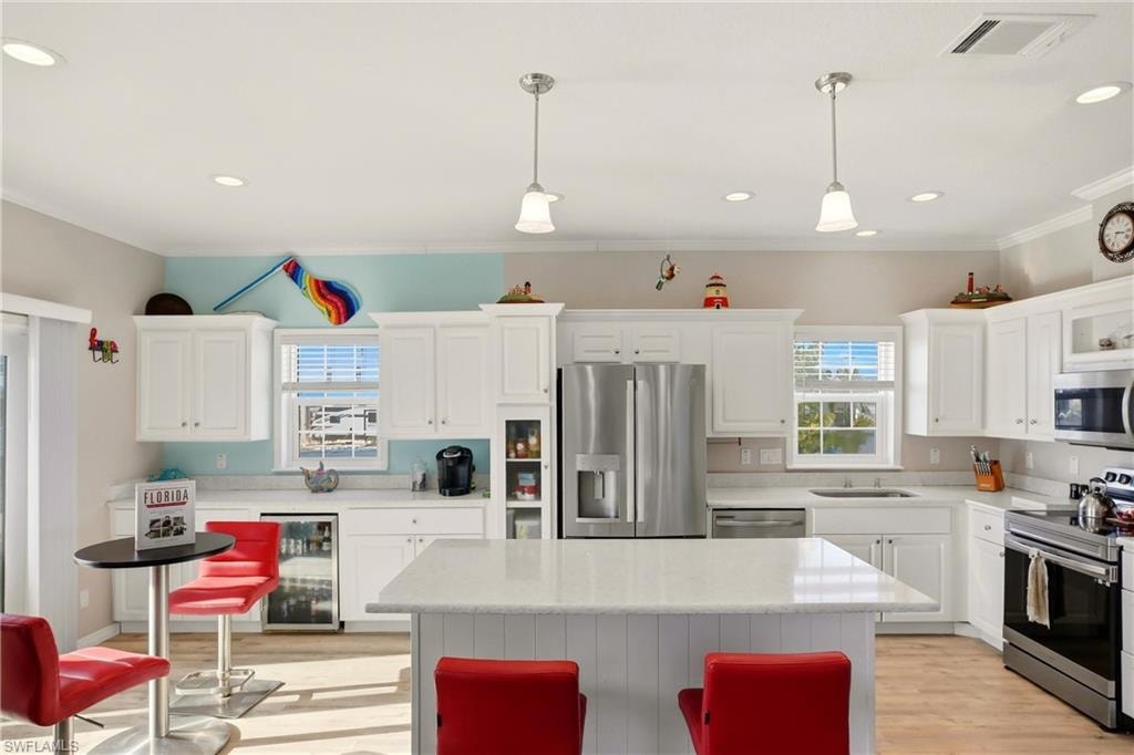 Kitchen with appliances with stainless steel finishes, wine cooler, white cabinets, decorative light fixtures, and crown molding