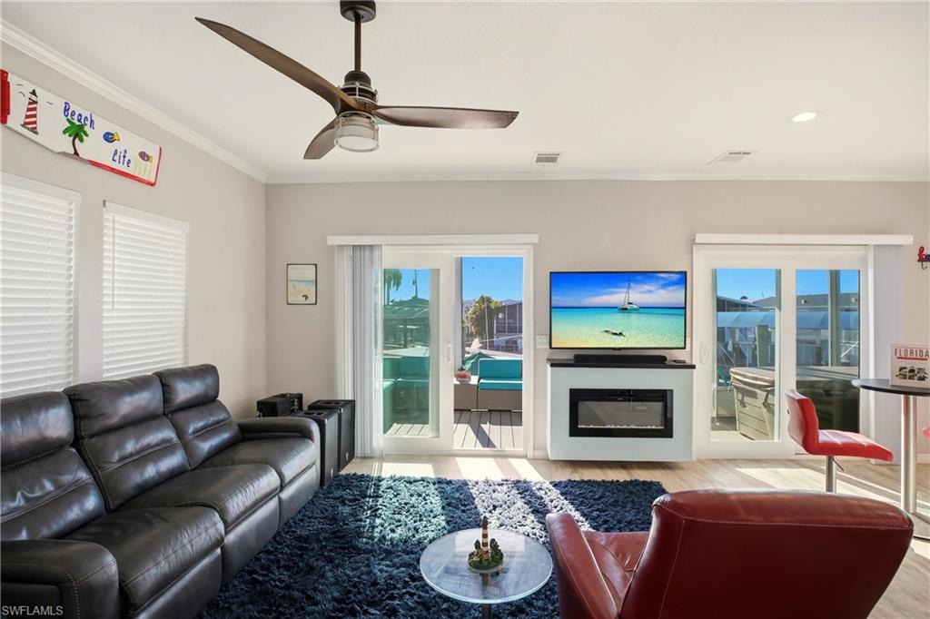 Living room with crown molding, light wood-style flooring, a glass covered fireplace, and a ceiling fan