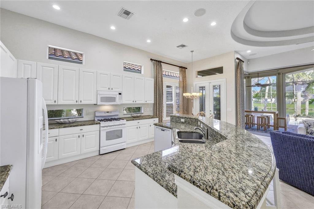 Kitchen featuring white cabinetry, light tile patterned floors, a center island with sink, and white appliances