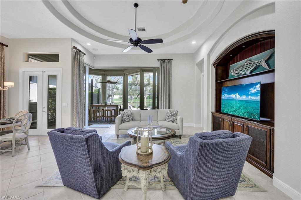 Tiled living room featuring ceiling fan, a raised ceiling, and french doors