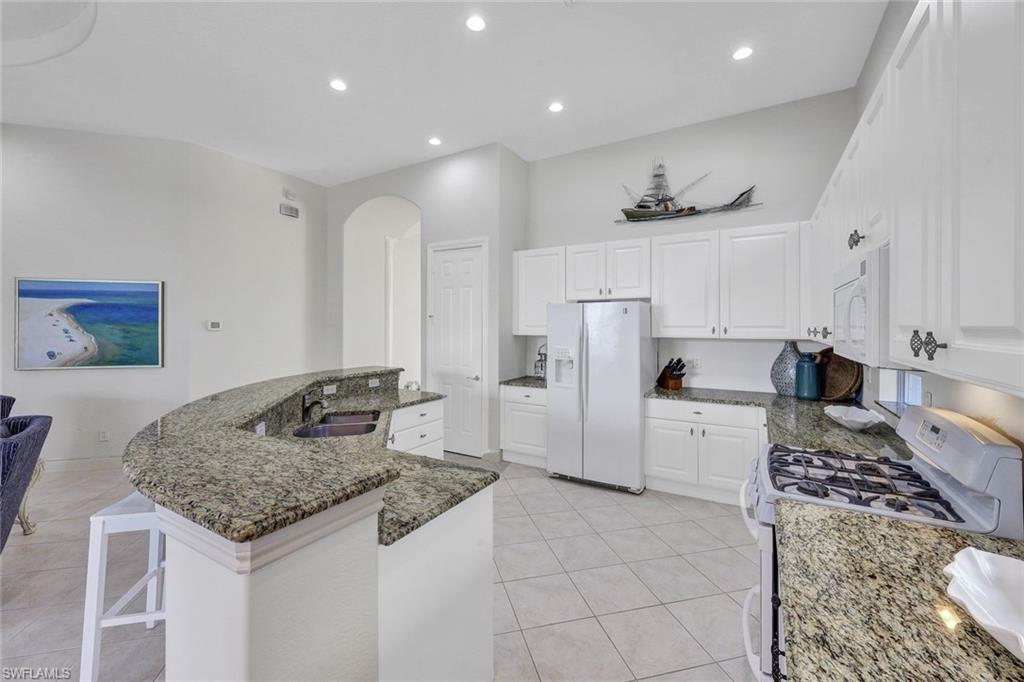 Kitchen with white cabinets, sink, white appliances, and light tile patterned floors