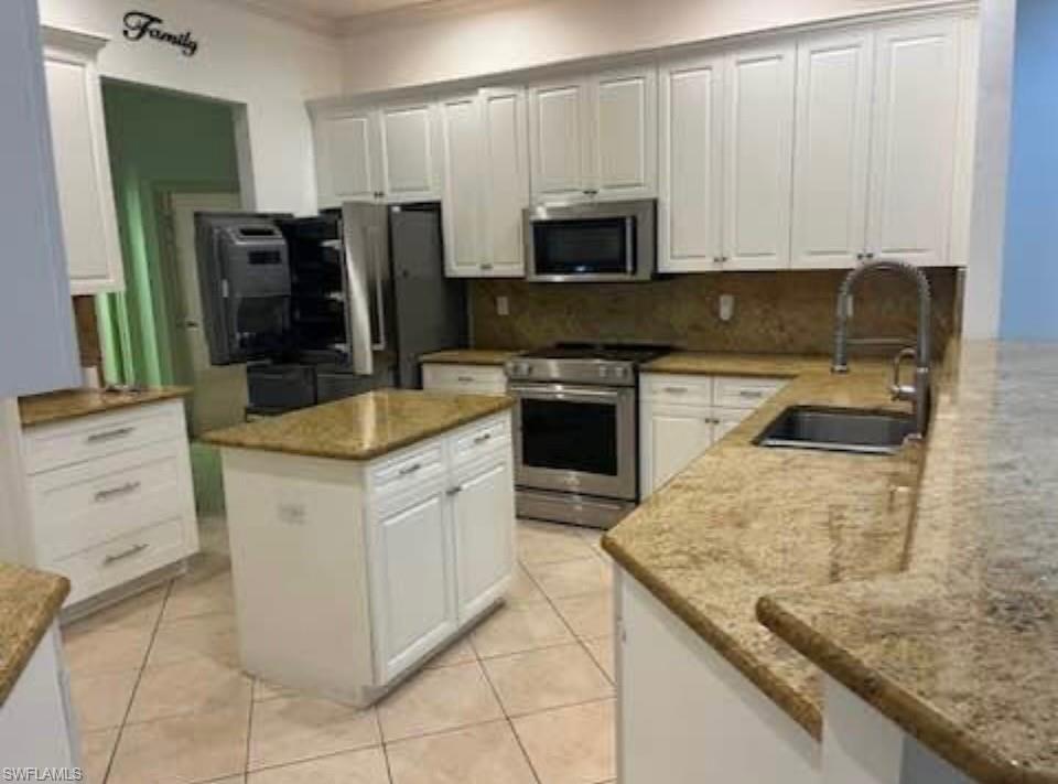 Kitchen with white cabinets, appliances with stainless steel finishes, light stone counters, a center island, and light tile patterned floors