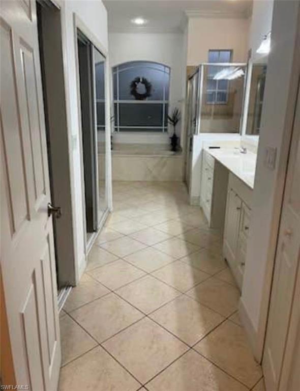 Bathroom featuring a stall shower, vanity, a garden tub, light tile patterned floors, and crown molding