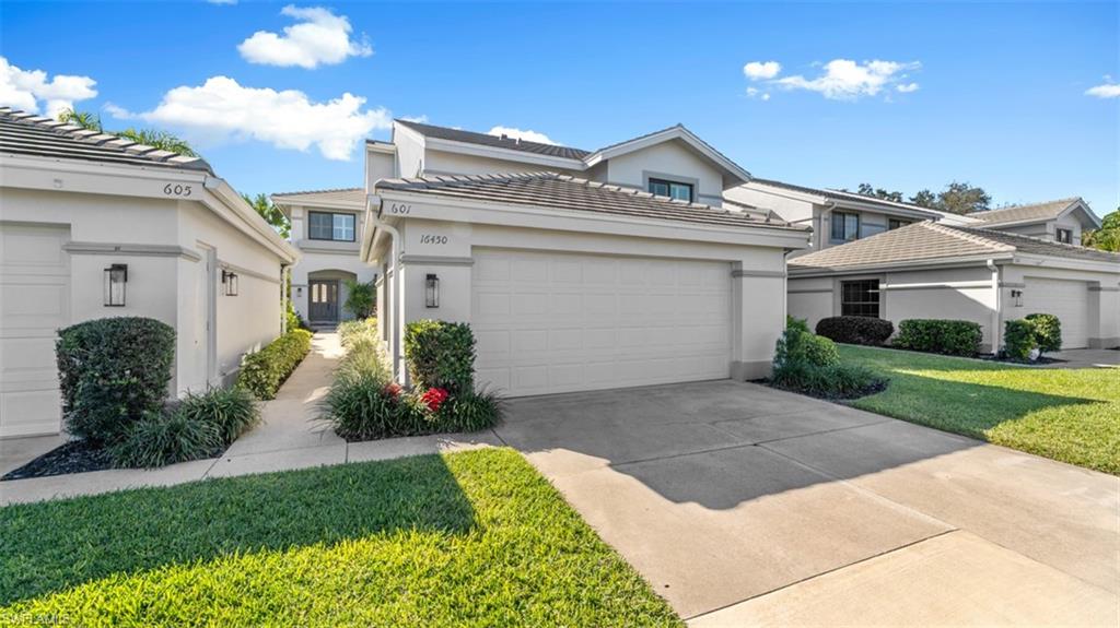 View of front facade featuring stucco siding, a front lawn, concrete driveway, and a tiled roof